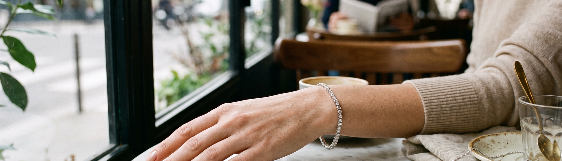 Woman's wrist wearing a natural diamond bracelet with a diamond necklace on a marble table