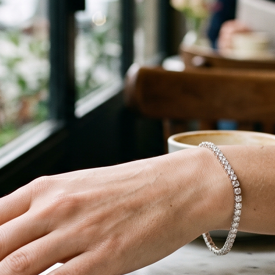 Woman's wrist wearing a natural diamond bracelet with a diamond necklace on a marble table