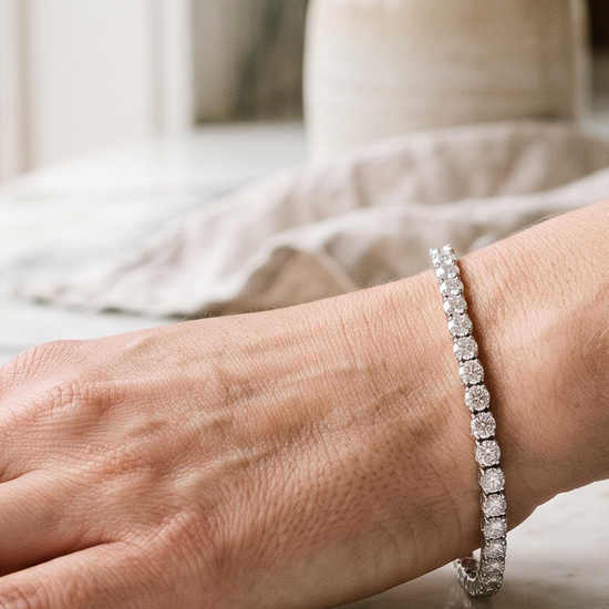 Woman's wrist wearing a lab-grown diamond tennis bracelet next to diamond stud earrings in natural light
