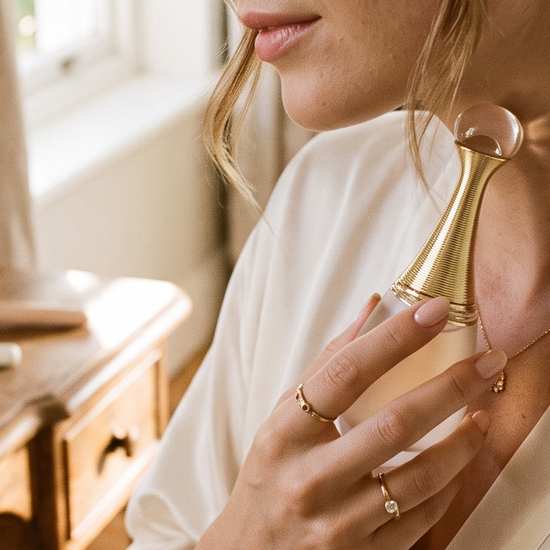 Woman holding a luxury perfume bottle while getting ready in a sunlit room