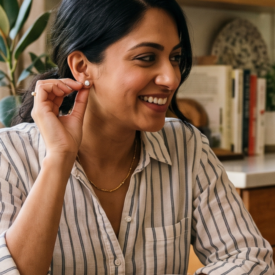 Two women laughing over chai at a sunlit kitchen table while one touches a diamond stud earring