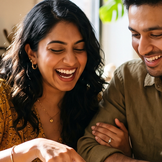 A couple laughing over chai while comparing engagement ring options on a tablet